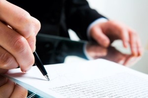 Closeup of business lady?s hand with pen signing a contract on the background of her other hand touching the table